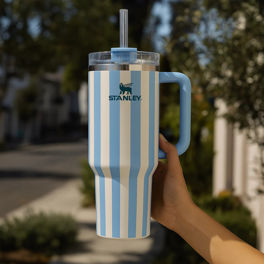 Blue and white striped Stanley tumbler held outdoors with trees in the background
