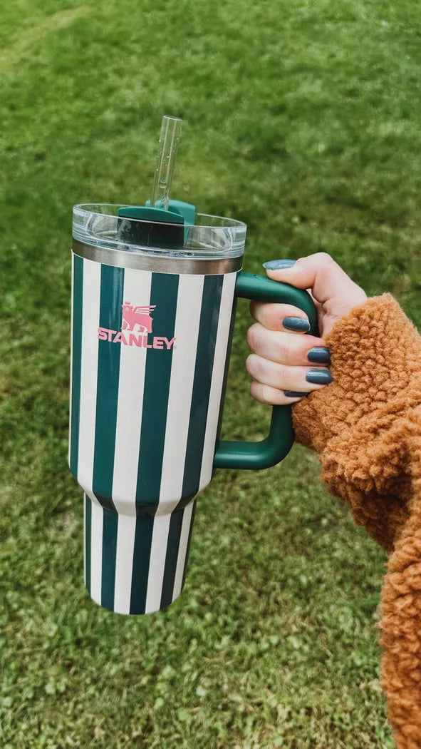Hand holding a striped Stanley tumbler on grass