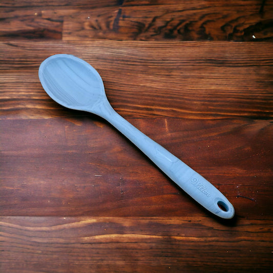 A blue silicone spoon with a long handle laid out on a wooden surface.