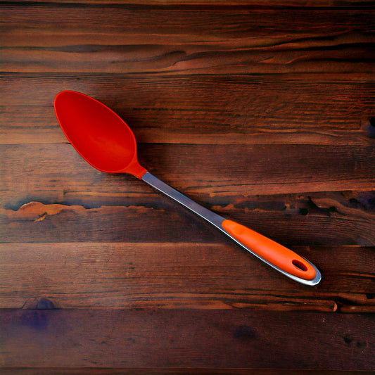 An orange silicone spoon with a stainless steel handle lying on a wooden surface.