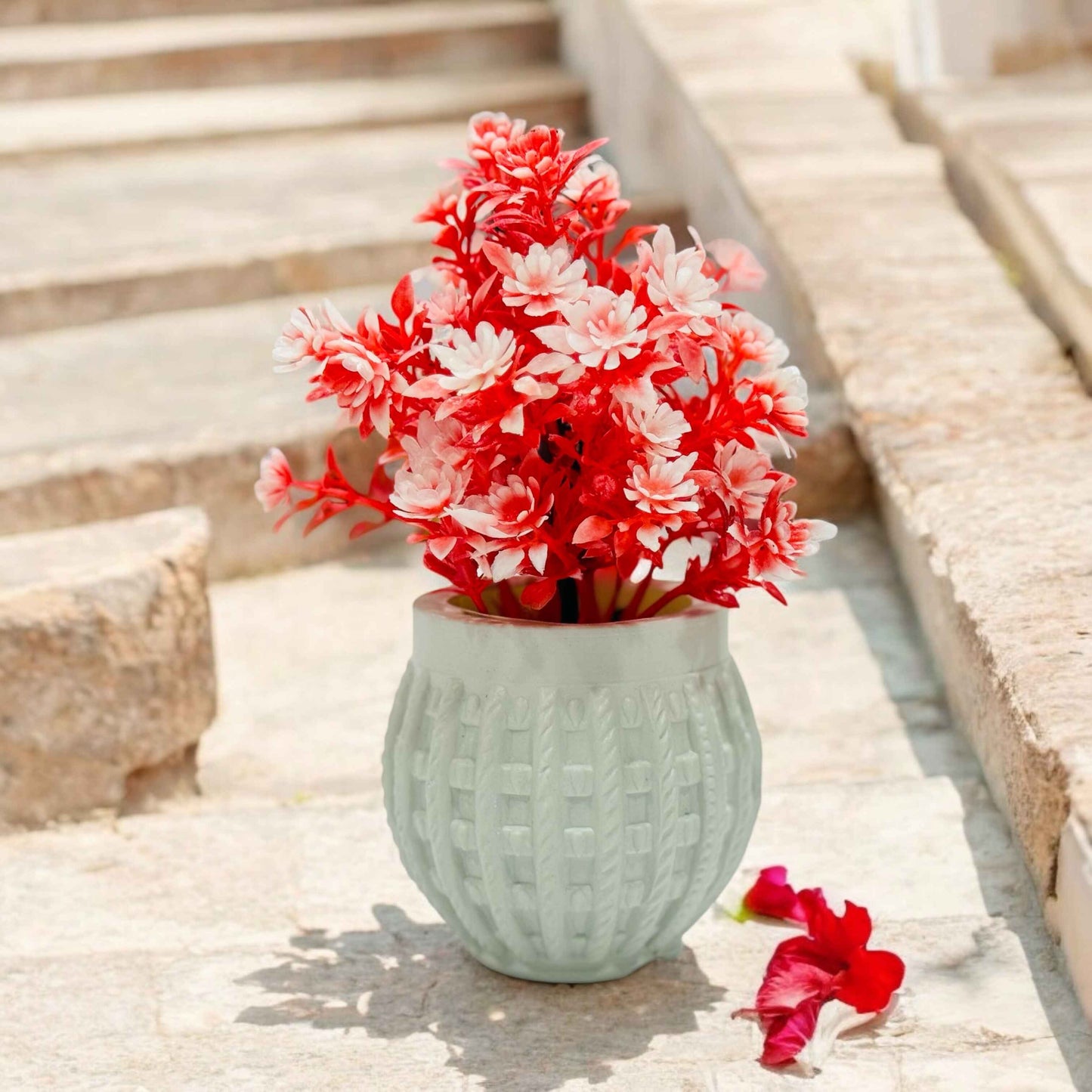White vase with red and pink flowers on a wooden surface