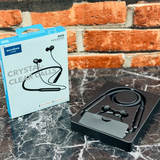 Black wireless earbuds with packaging on a marble surface against a brick wall background
