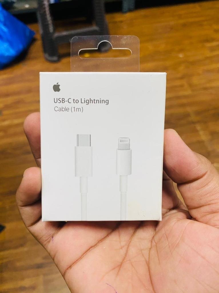 Apple USB-C to Lightning cable packaging held in a hand on a wooden surface
