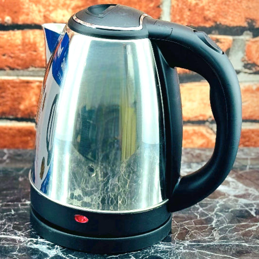 electric kettle on a stovetop with a black handle and a red indicator light visible.