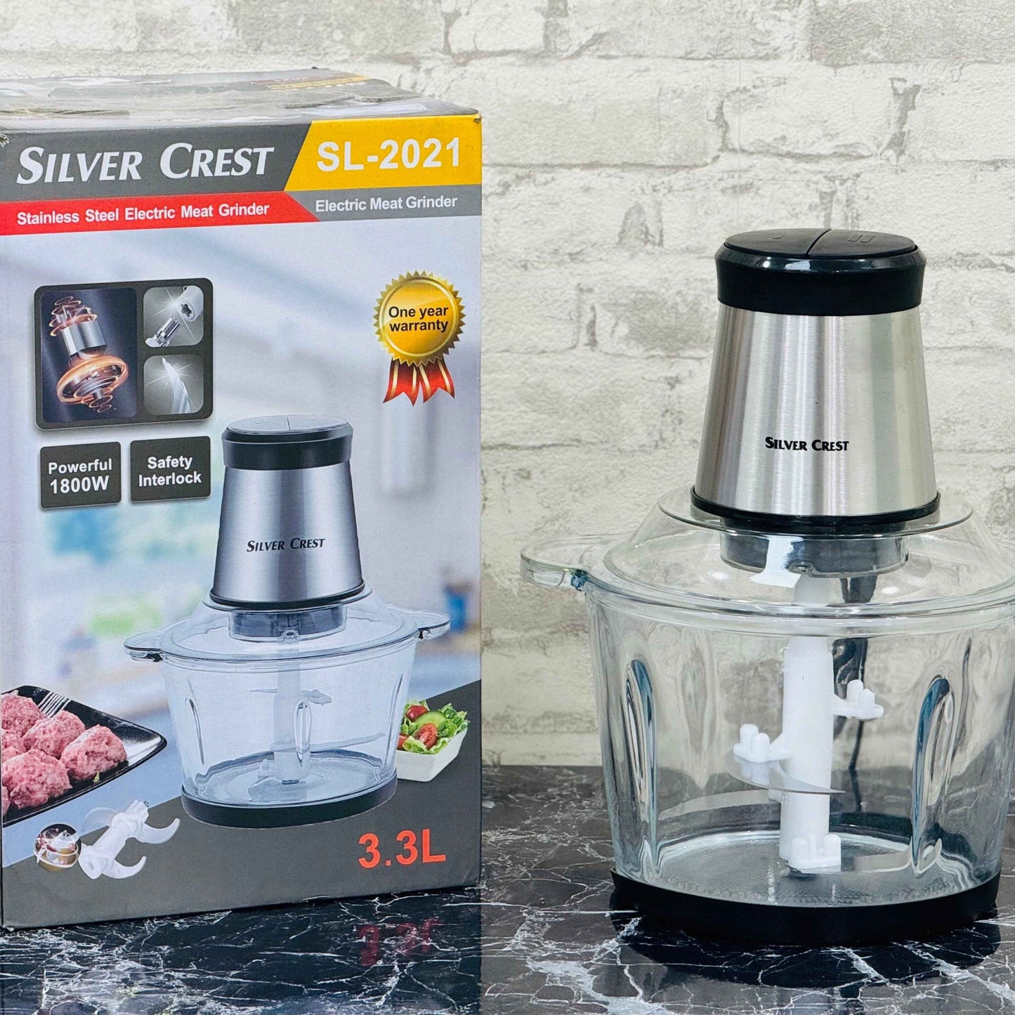 Silver Crest electric chopper in a 3.3 liter glass bowl, with packaging box and a manual, on a kitchen counter.