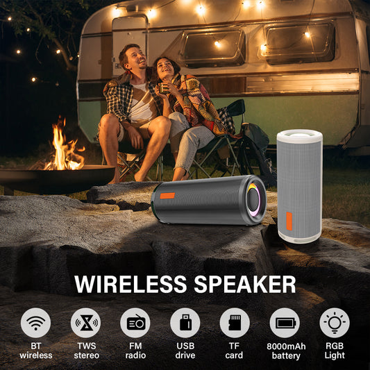 Two people sitting by a campfire with a wireless speaker and a portable device on a rock, with a camper in the background.