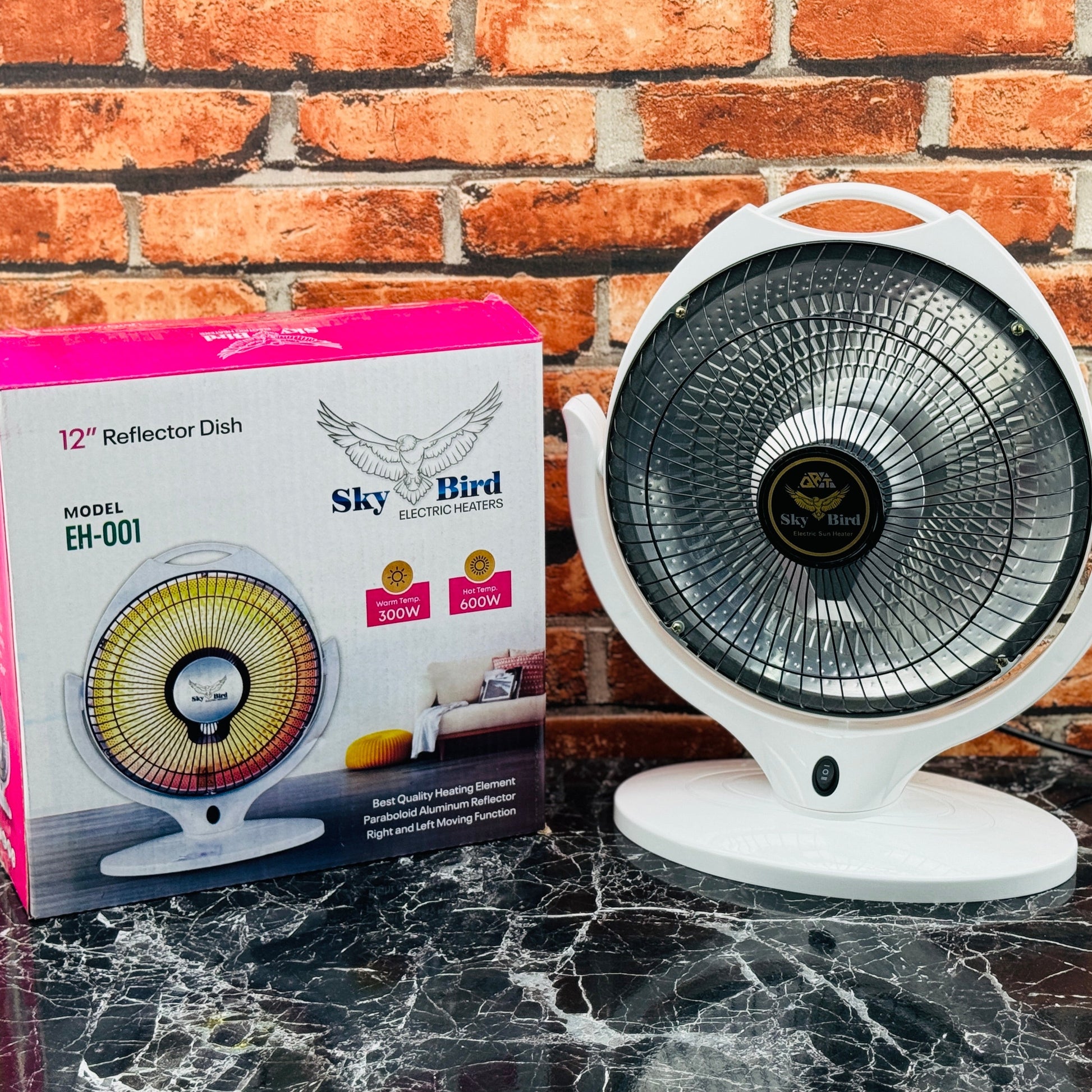 A 12-inch Sky Bird reflector dish heater with a silver spray net cover, displayed next to its packaging box on a marble surface with a pink brick wall in the background.