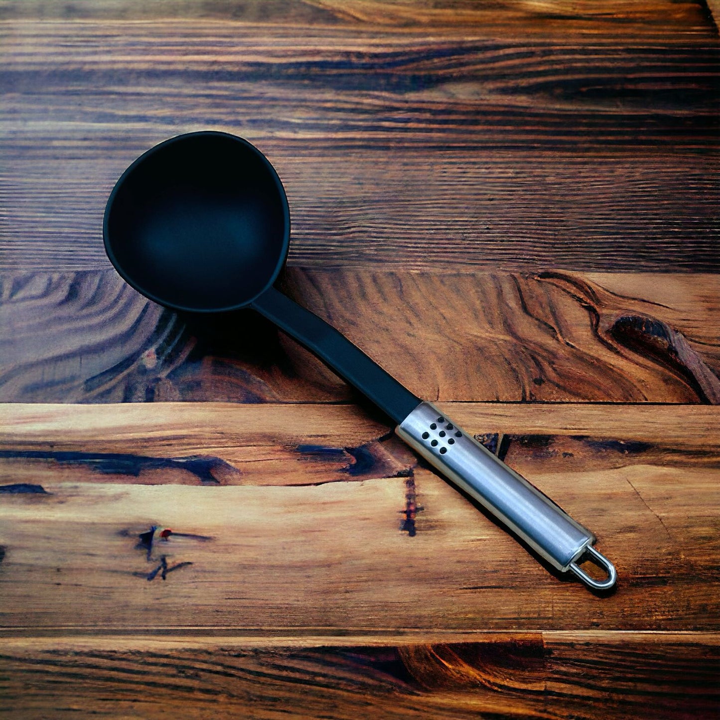 A black nylon soup ladle with a stainless steel handle lying on a wooden surface.