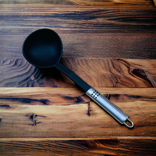 A black nylon soup ladle with a stainless steel handle lying on a wooden surface.