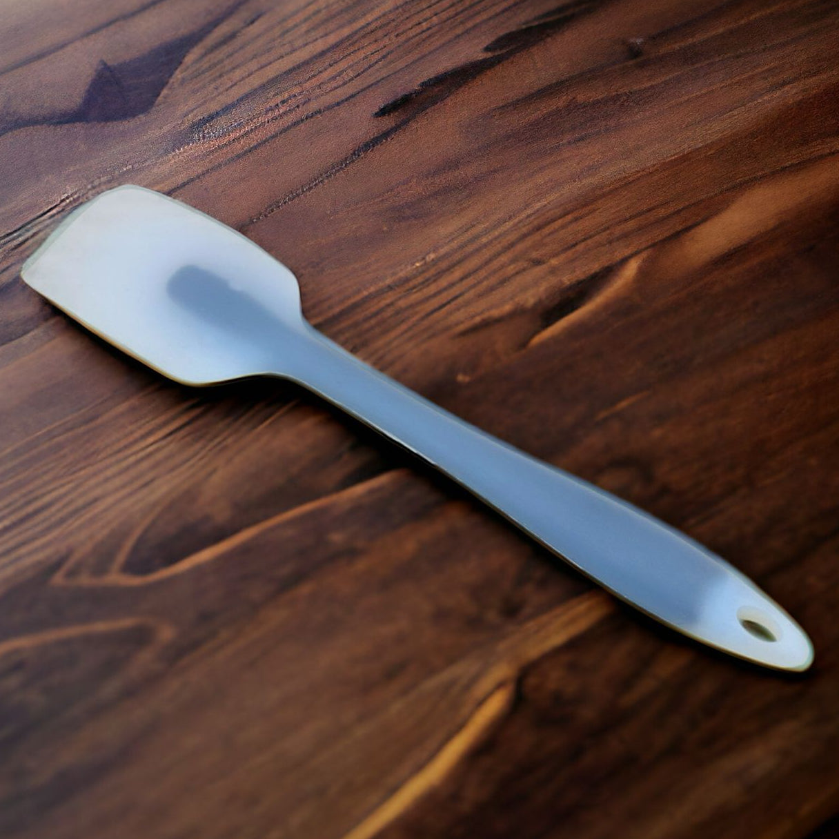 A silicone cream scraper with a white tip lying on a wooden surface.