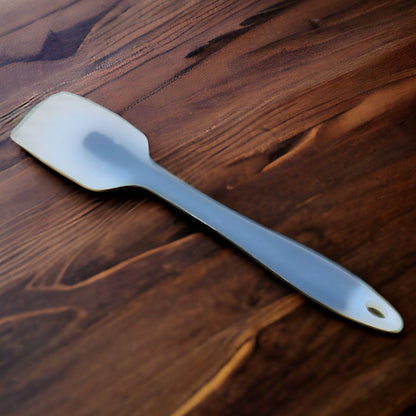 A silicone cream scraper with a white tip lying on a wooden surface.