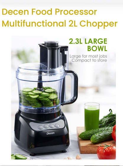 Decen food processor with a large bowl containing sliced cucumbers, surrounded by vegetables and a glass of green juice.
