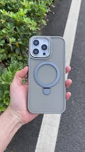 Hand holding a phone with a case and ring holder on a road.