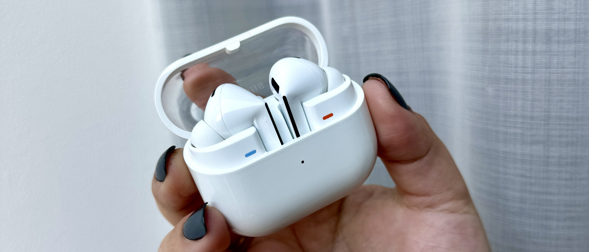 Hand holding a white wireless earbud case with earbuds inside against a light background