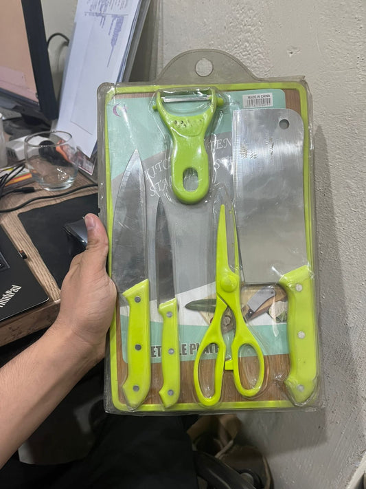 Set of kitchen utensils including knives and a peeler in packaging on a desk.