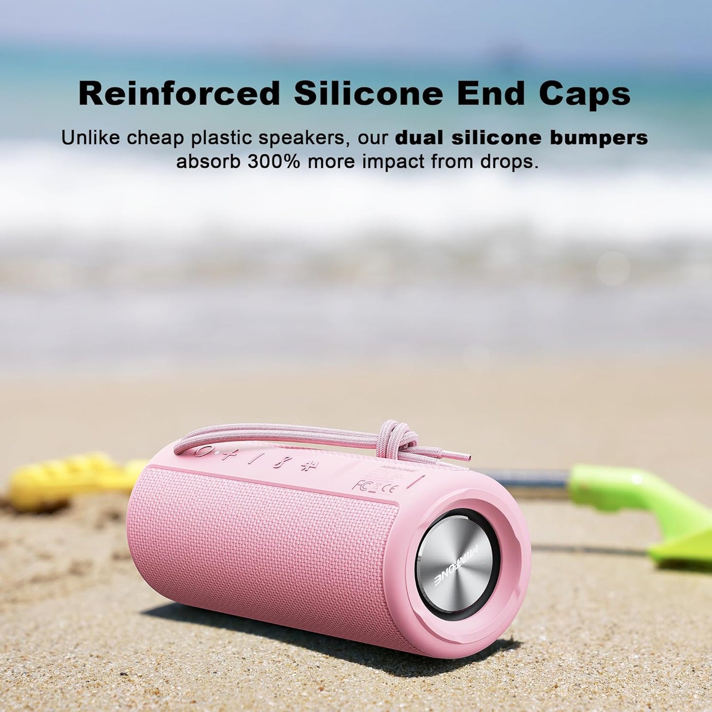 Pink portable speaker with reinforced silicone end caps on a sandy beach.