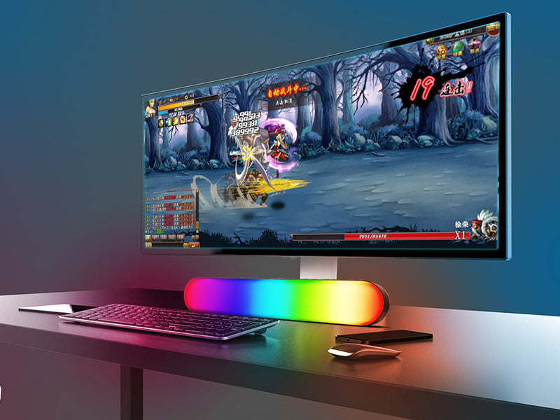 Gaming setup with a monitor displaying a game, keyboard, and RGB mouse pad on a desk.