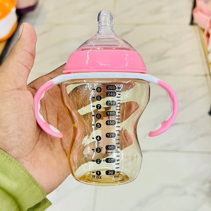 Baby bottle with pink handle and clear body showing measurement markings held by a hand.