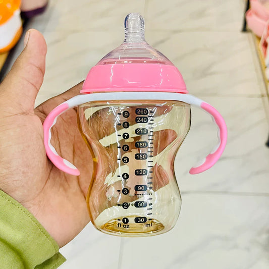 Baby bottle with pink handle and clear body showing measurement markings held by a hand.