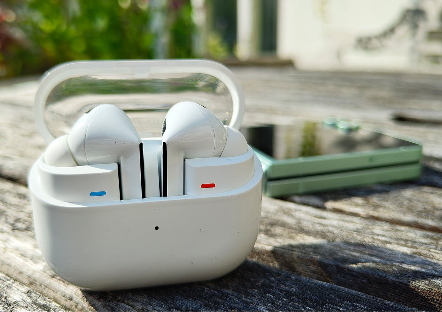 White wireless earbuds in a transparent case on a wooden surface with a blurred natural background