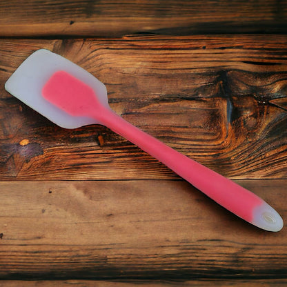 A red silicone cream scraper with a white tip lying on a wooden surface.