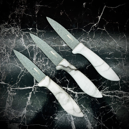 A set of three kitchen knives with Japanese stainless steel blades and white marble-like handles, displayed on a dark marble surface.