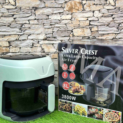 Green air fryer with Silver Crest packaging against a stone wall background