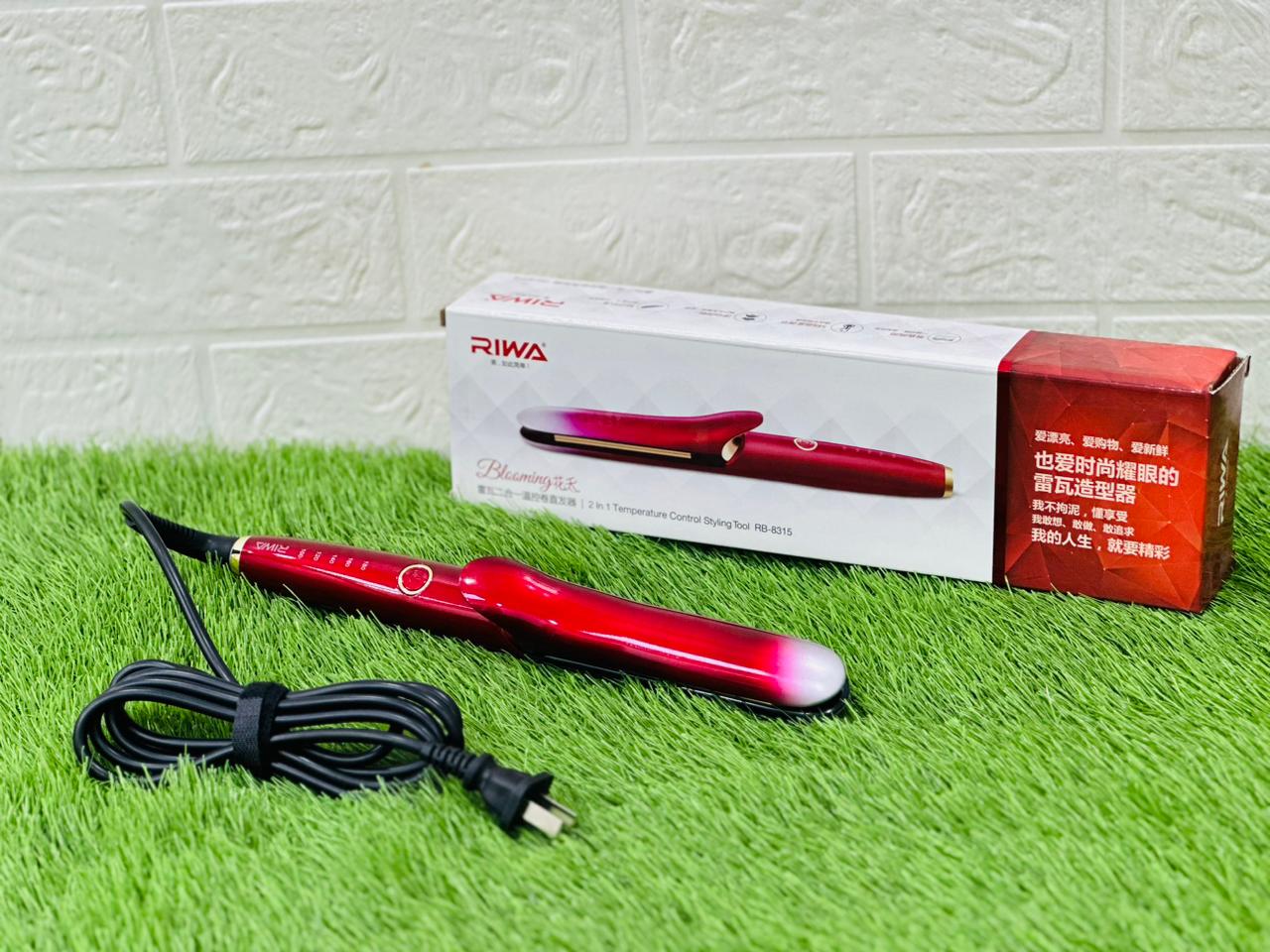 A Riwa hair straightener with a red and black design, displayed alongside its packaging and a power cord, placed on a green mat.