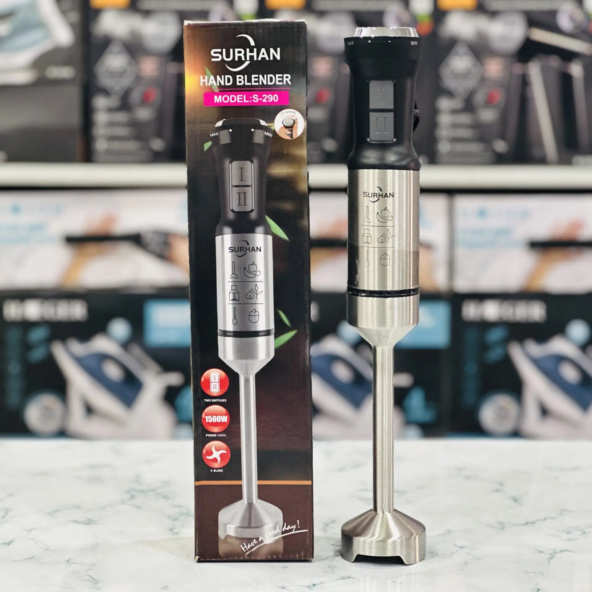 A Surhan hand blender displayed alongside its packaging, featuring a stainless steel design with a silver color, showcasing the product and its box with brand and product information.